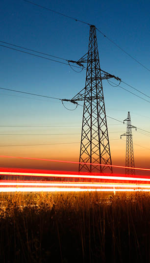 Pylons and electricity powerlines at night with traffic lights in front