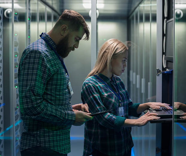Diverse adult man and woman using tablet and laptop while diagnosing server hardware in modern data center