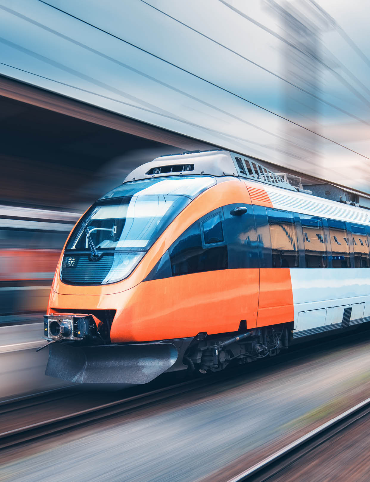 High speed orange train in motion on the railway station at sunset. Modern intercity passenger train with motion blur effect on the railway platform. Industrial. Railroad in Europe. Transport