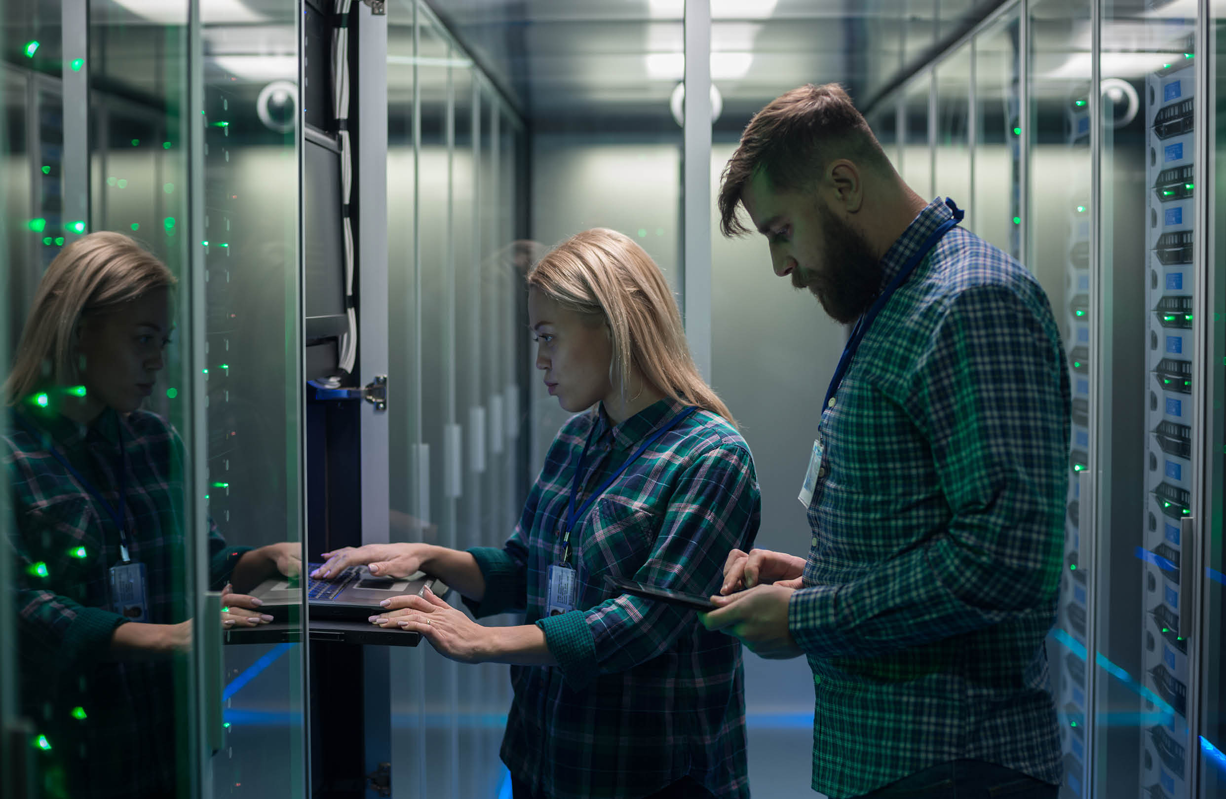 Diverse adult man and woman using tablet and laptop while diagnosing server hardware in modern data center